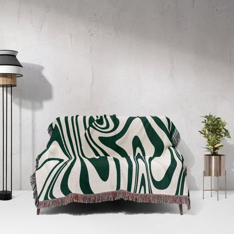 Sofa with an abstract patterned forest green marble woven throw blanket for couch against a white wall.