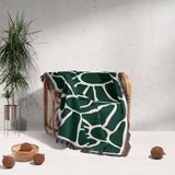 Forest green Matisse tapestry throw blanket for couch draped over a chair with a plant and coconuts in the background.