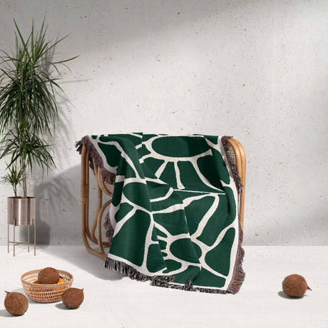 Forest green Matisse tapestry throw blanket for couch draped over a chair with a plant and coconuts in the background.
