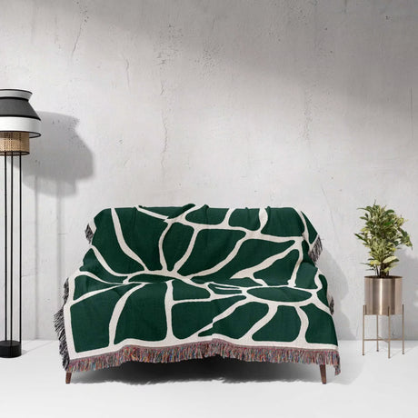 Forest green Matisse tapestry throw blanket for couch draped over a couch against a white wall.