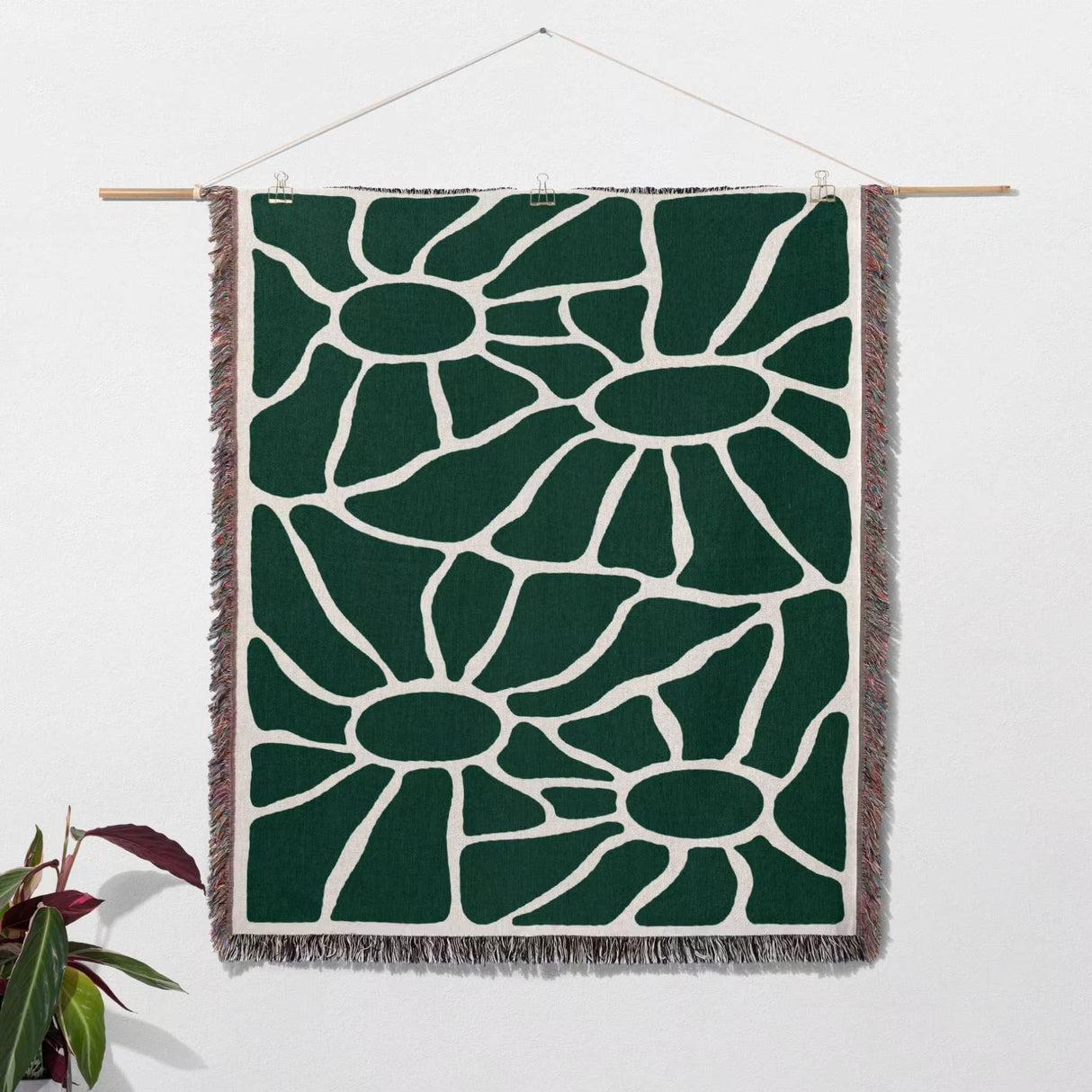 Forest green Matisse tapestry throw blanket for couch as a wall hanging on a white wall with a plant in the corner.
