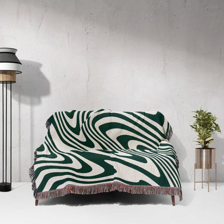 Aesthetic forest green modern decorative woven throw blanket draped over a couch against a white wall.