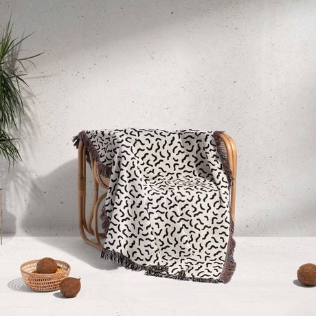 Woven chair with a funky squiggly woven blanket throw tapestry on a light background