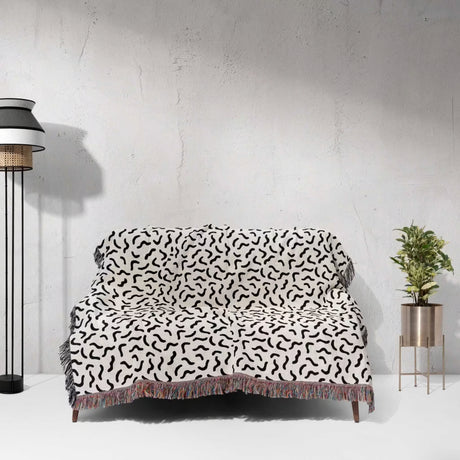Sofa with a black and white funky squiggly woven blanket throw tapestry against a white wall.
