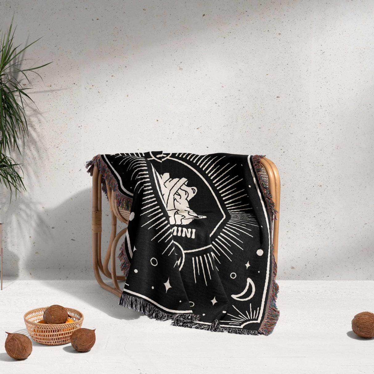 The Gemini Zodiac Blanket artistically draped over a chair, highlighting its versatility and decorative appeal. The black and off-white design with celestial symbols complements the chair and surrounding decor.