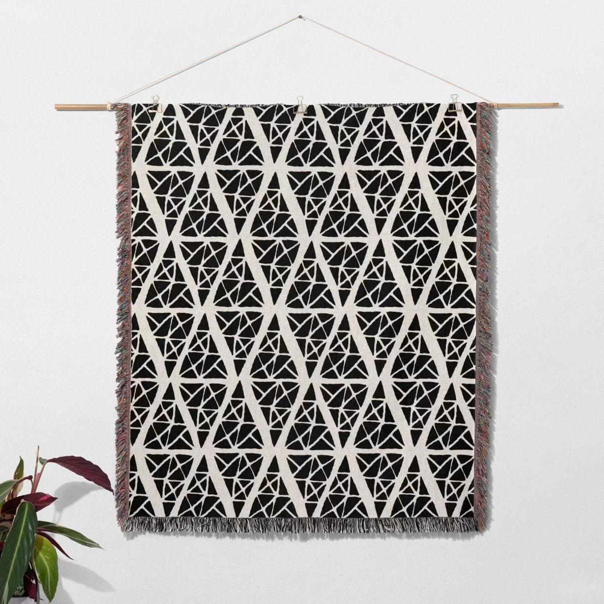 Black and white triangle patterned geometric patterned woven blanket throw tapestry with fringe hanging on a wooden rod against a white wall.