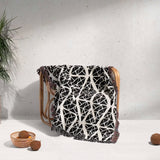 Geometric patterned woven blanket throw tapestry blanket draped over a wooden chair against a light gray wall.