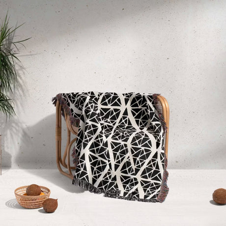 Geometric patterned woven blanket throw tapestry blanket draped over a wooden chair against a light gray wall.