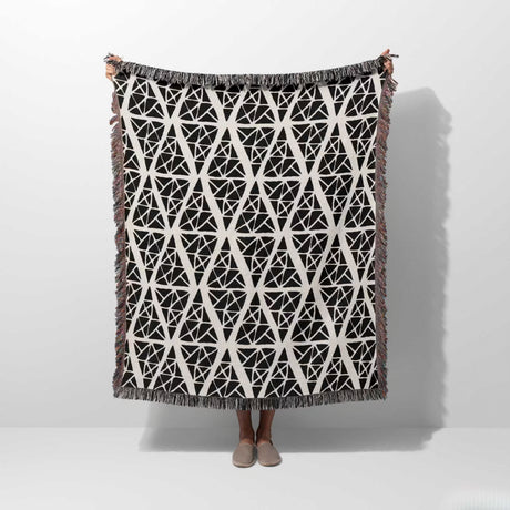 Geometric patterned woven blanket throw tapestry with geometric pattern on a white background held by a person. 
