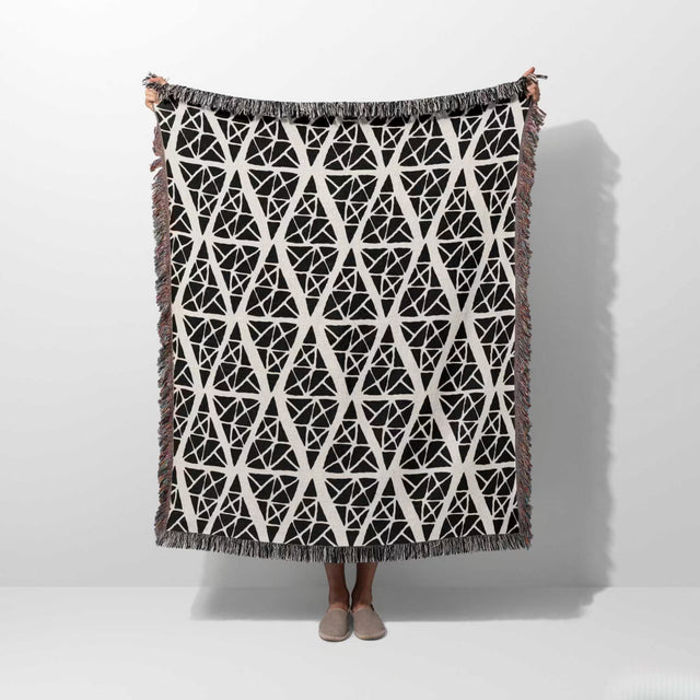 Geometric patterned woven blanket throw tapestry with geometric pattern on a white background held by a person. 