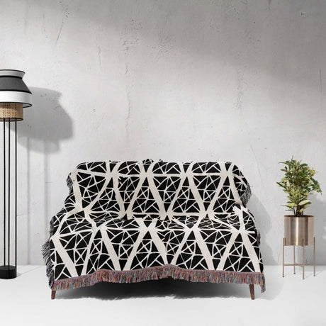Black and white patterned geometric patterned woven blanket throw tapestry on a sofa against a white wall.