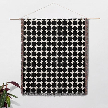 Black and white geometric square patterned woven blanket throw hanging on a wooden rod against a white background.