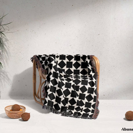 Black and white geometric square patterned woven blanket throw draped over a wooden chair against a light background.
