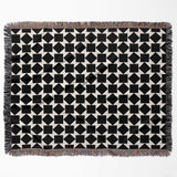 Black and white geometric square patterned woven blanket throw with fringed edges flat lay on a white background.