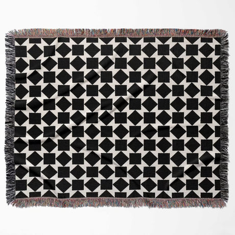 Black and white geometric square patterned woven blanket throw with fringed edges flat lay on a white background.