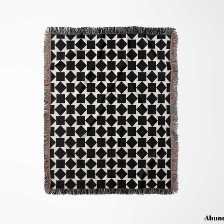 Black and white geometric square patterned woven blanket throw full view with fringe on a light gray background.