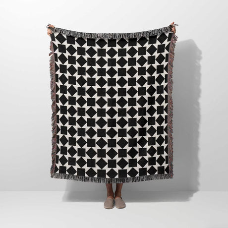 Black and white geometric square patterned woven blanket throw held by a person on a white background.