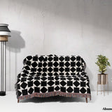 Black and white geometric square patterned woven blanket throw draped over a sofa against a white wall.