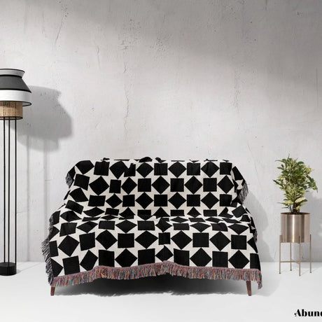Black and white geometric square patterned woven blanket throw draped over a sofa against a white wall.