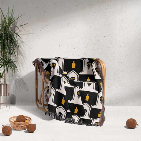 Decorative blanket with black and white pattern draped over a chair against a light gray wall.