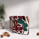 Decorative Henri Matisse red flowers woven throw blanket with leaf pattern draped over a chair against a light gray wall.