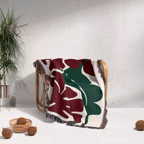 Decorative Henri Matisse red flowers woven throw blanket with leaf pattern draped over a chair against a light gray wall.