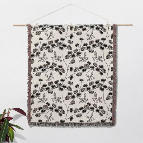 Japanese style woven blanket throw tapestry with bird and branch pattern hanging on a white wall.