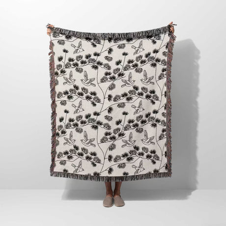 Person holding a decorative Japanese style woven blanket throw tapestry with black floral and bird pattern on a white background.