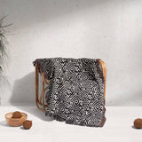 Black and white labyrinth hexagon pattern woven blanket throw cover ing a wooden chair against a white wall.