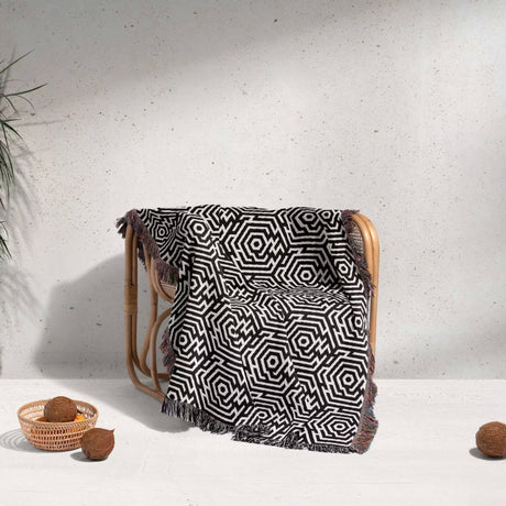 Black and white labyrinth hexagon pattern woven blanket throw cover ing a wooden chair against a white wall.