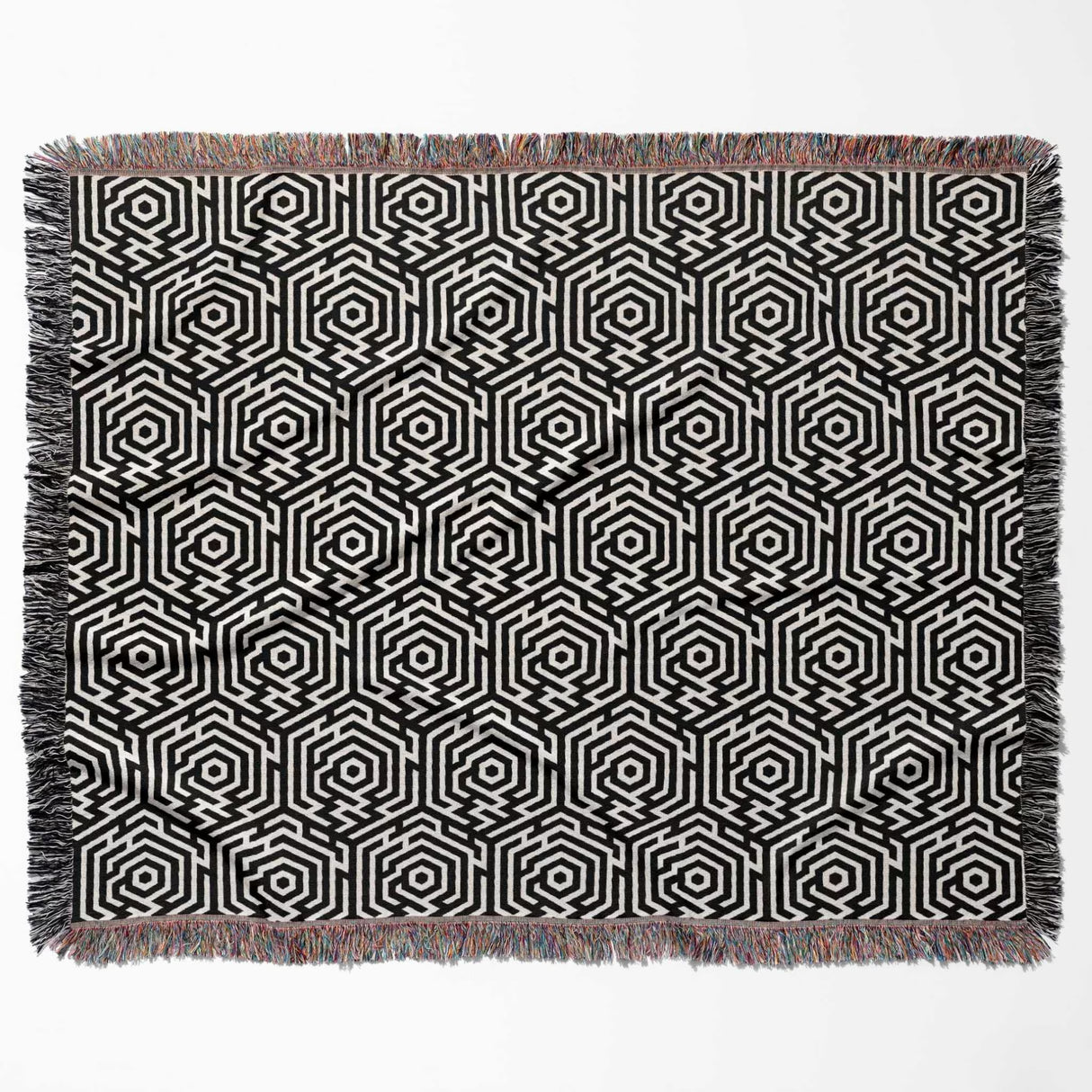 Black and white labyrinth hexagon pattern woven blanket throw with fringe flat lay on a white background.