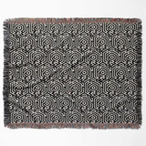 Black and white labyrinth hexagon pattern woven blanket throw with fringe flat lay on a white background.
