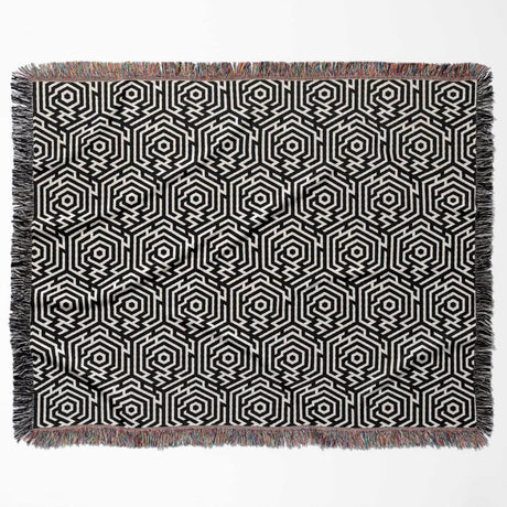 Black and white labyrinth hexagon pattern woven blanket throw with fringe flat lay on a white background.