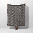 Black and white labyrinth hexagon pattern woven blanket throw held by a person on a white background.