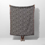 Black and white labyrinth hexagon pattern woven blanket throw held by a person on a white background.