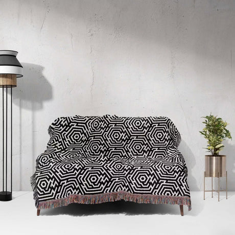 Black and white labyrinth hexagon pattern woven blanket throw on a sofa against a white wall.