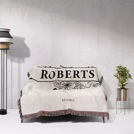 Last name monogram blanket with 'ROBERTS' and 'EST. 2022' text draped over a couch against a white wall.