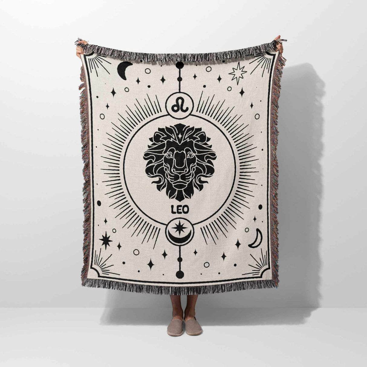 This image features a person holding a Leo Zodiac Blanket vertically, displaying the intricate lion design. The woven throw tapestry showcases a detailed black-and-white illustration with celestial elements, perfect for astrology enthusiasts and home decor.