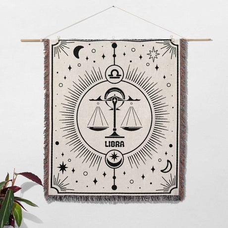 Libra Zodiac Blanket displayed as wall art decor, demonstrating its versatility as both a decorative tapestry and functional throw. The detailed black design on an off-white woven cotton base makes it a perfect birthday gift for astrology lovers looking to enhance their home decor.