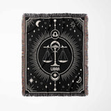 The Libra Zodiac Blanket displayed flat in a vertical orientation, highlighting the intricate woven details and the balance scales symbol of Libra, with decorative elements of the night sky and a multicolor fringe that frames the blanket.