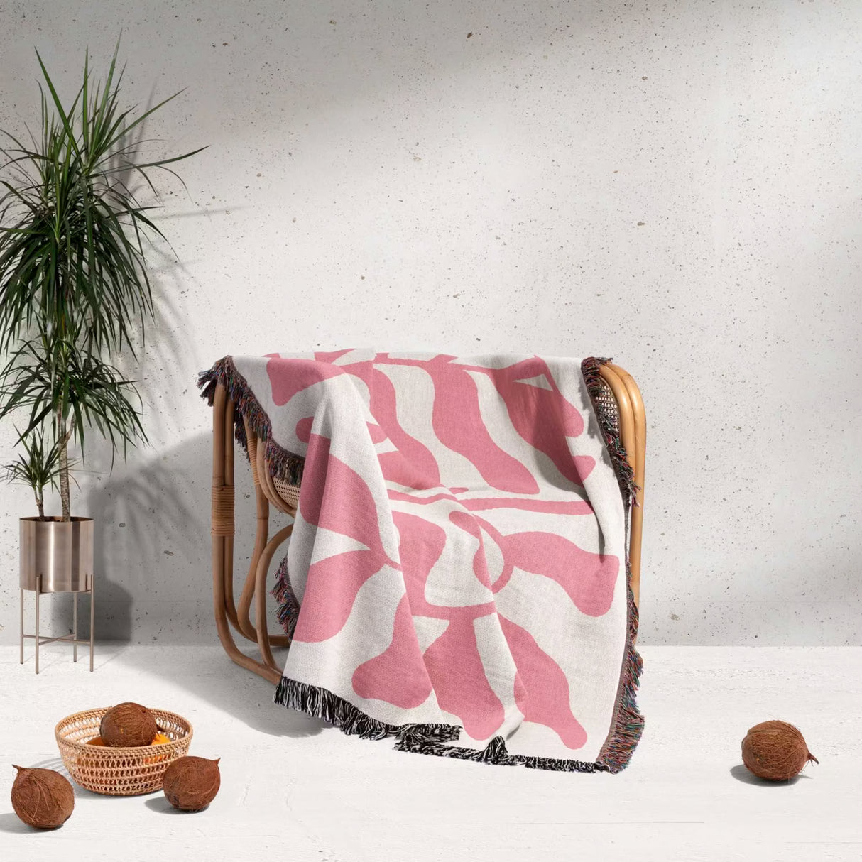 Lighter red leaf Matisse throw blanket draped over a chair with a plant and coconuts in the background.