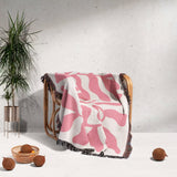 Lighter red leaf Matisse throw blanket draped over a chair with a plant and coconuts in the background.