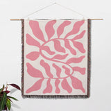 Lighter red leaf Matisse throw blanket hanging on a wooden rod against a white wall.