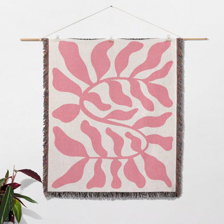 Lighter red leaf Matisse throw blanket hanging on a wooden rod against a white wall.