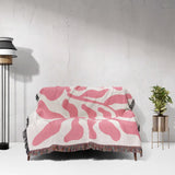 Lighter red leaf Matisse throw blanket draped over a couch against a white wall.