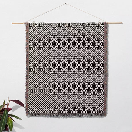 Black and white luxury geometric patterned woven blanket throw tapestry with hanging on a wooden rod against a white wall.