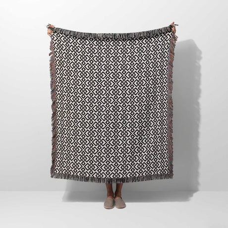 Black and white luxury geometric patterned woven blanket throw tapestry with fringes held by a person on a white background
