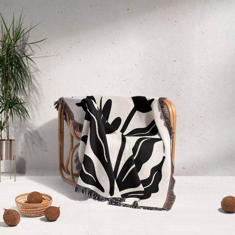 Matisse flowers black and white woven throw blanket draped over a chair against a light gray wall.
