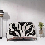 Black and white patterned Matisse flowers black and white woven throw blanket draped over a chair against a light gray wall.