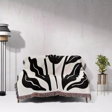Black and white patterned Matisse flowers black and white woven throw blanket draped over a chair against a light gray wall.